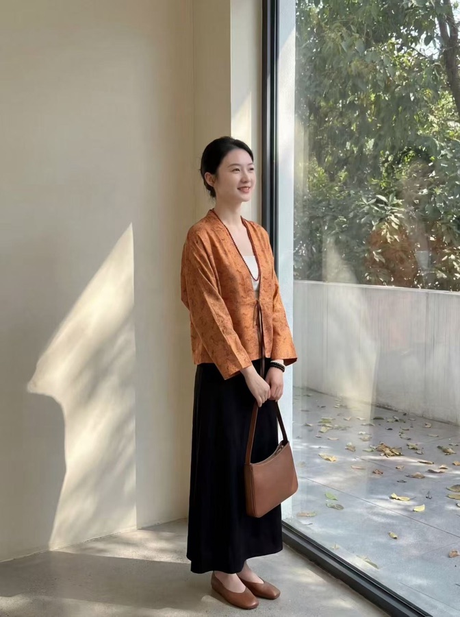 新中式风格真丝橘色对襟上衣搭配黑色半身裙模特实拍图，颜色搭配属于姜黄暖色加黑色沉稳色，秋冬通勤与出游穿搭参考